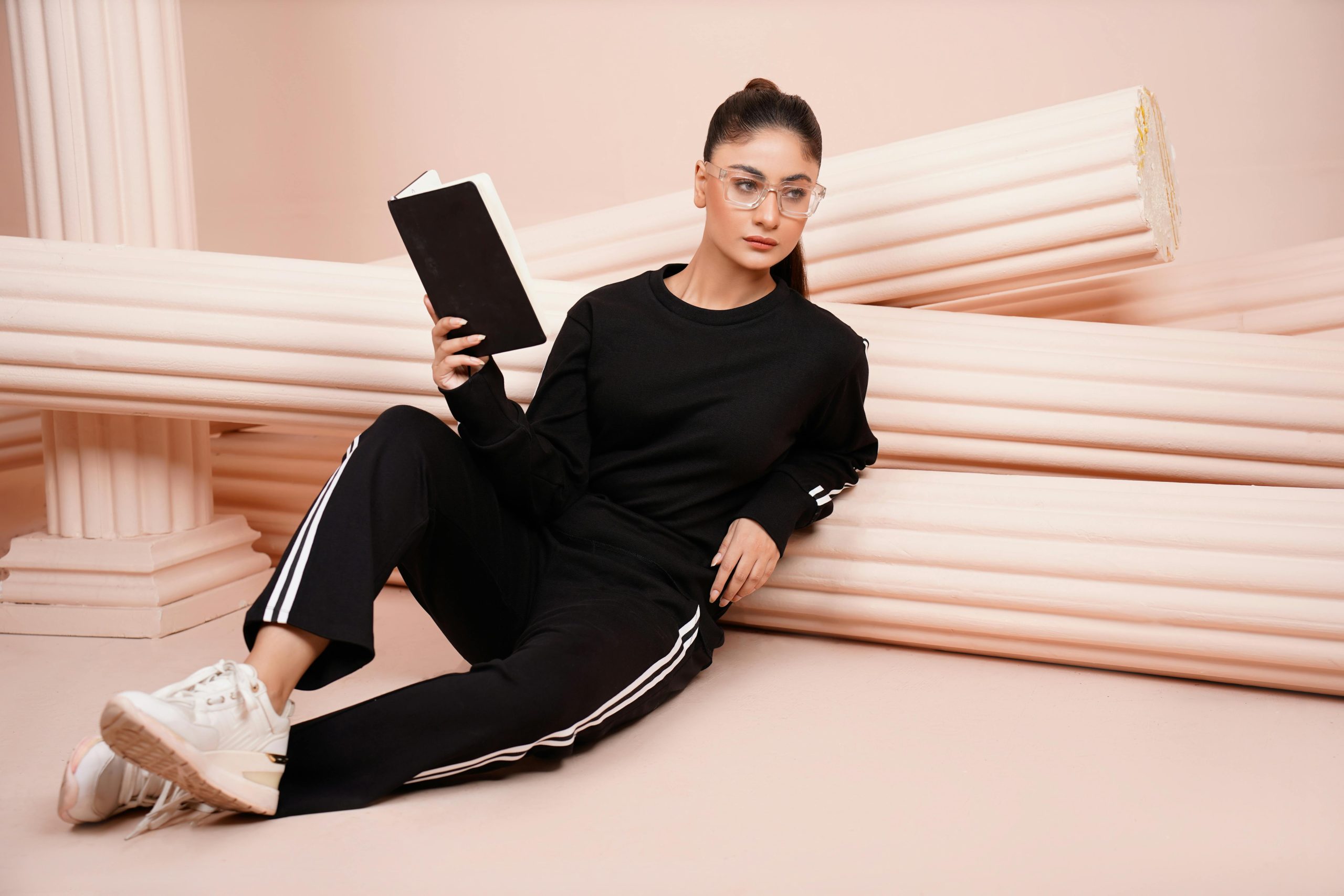 Woman in black athleisure holding a book against a classical column backdrop.